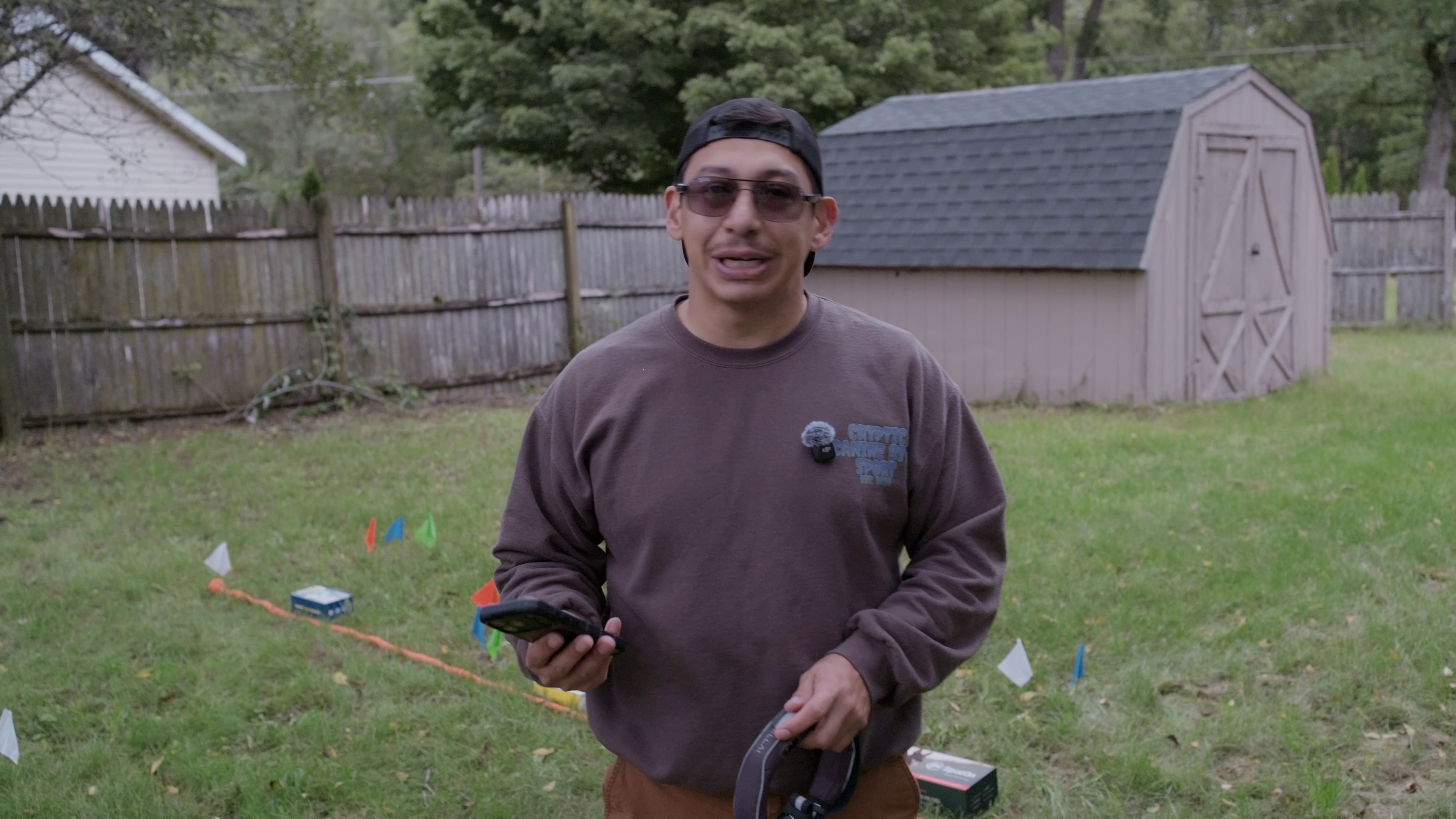 Lucas holding collar and phone at the testing site with colored flags marking correction points behind him